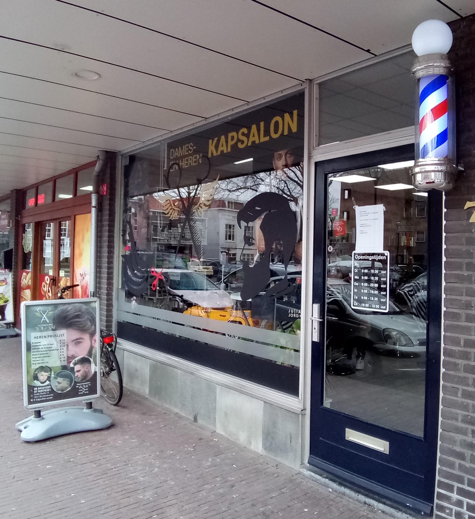De pui van Kapsalon Aryan overdag, met de kapperspaal naast de deur en het stoepbord met de prijslijst